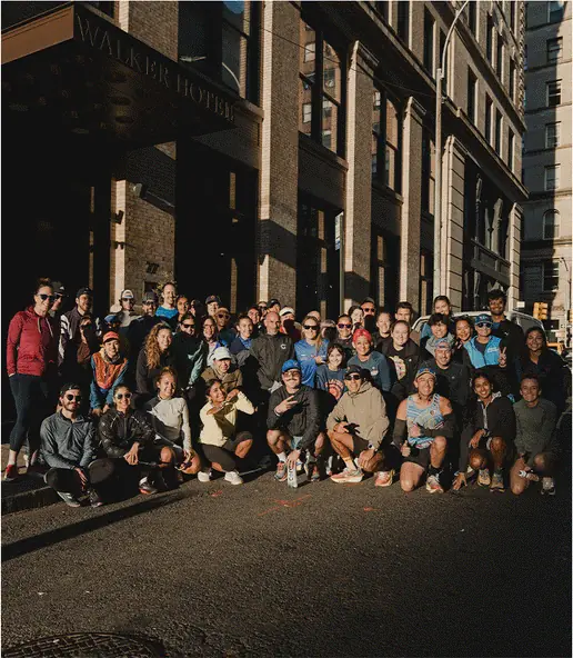 A big run club group posing on a sunlit street outside a hotel