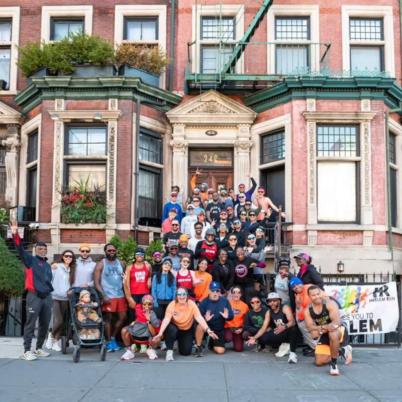 A big crowd of runners posing on a brownstone's steps