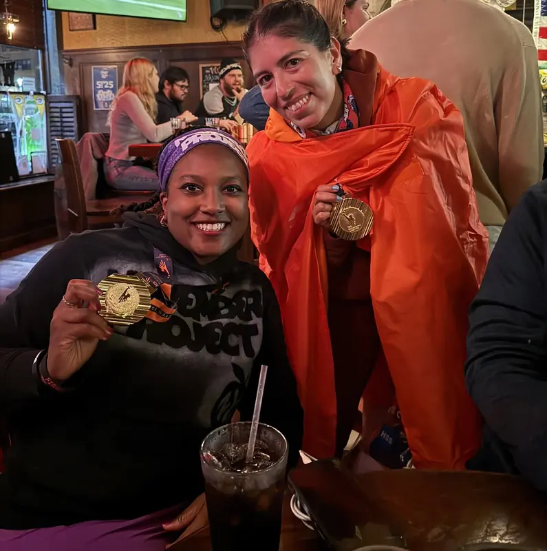 Two finishers in orange ponchos holding up their medals in a bar
