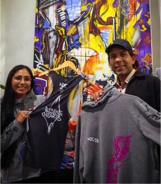 Two people holding up running shirts in front of a bright painting