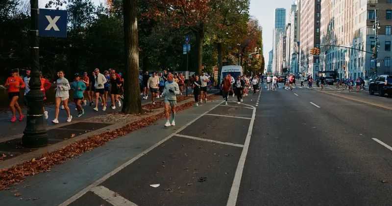 Marathoners running beside Central Park under autumn trees