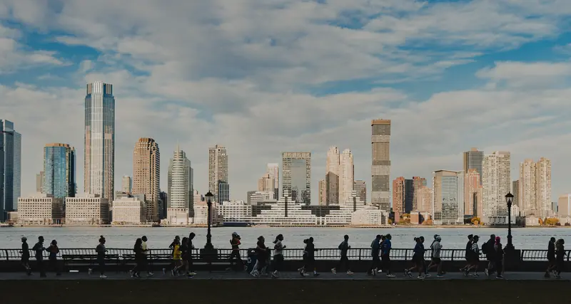 Runners in silhouette along the Hudson, a skyline across the water