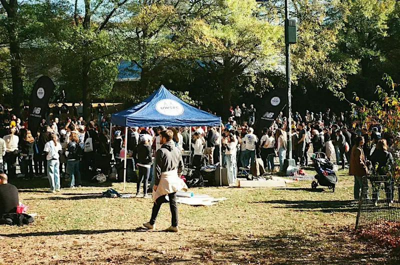 A crowd of runners gathered round a blue tent in a sunny park