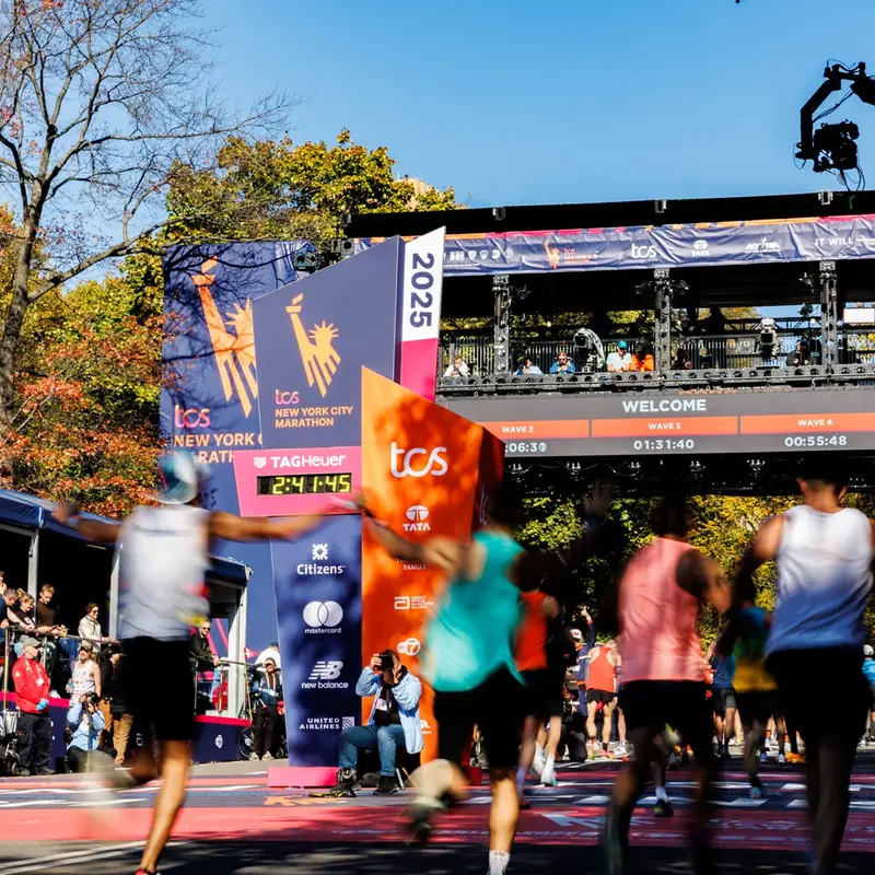 Runners crossing a marathon finish line under its arch, spectators either side